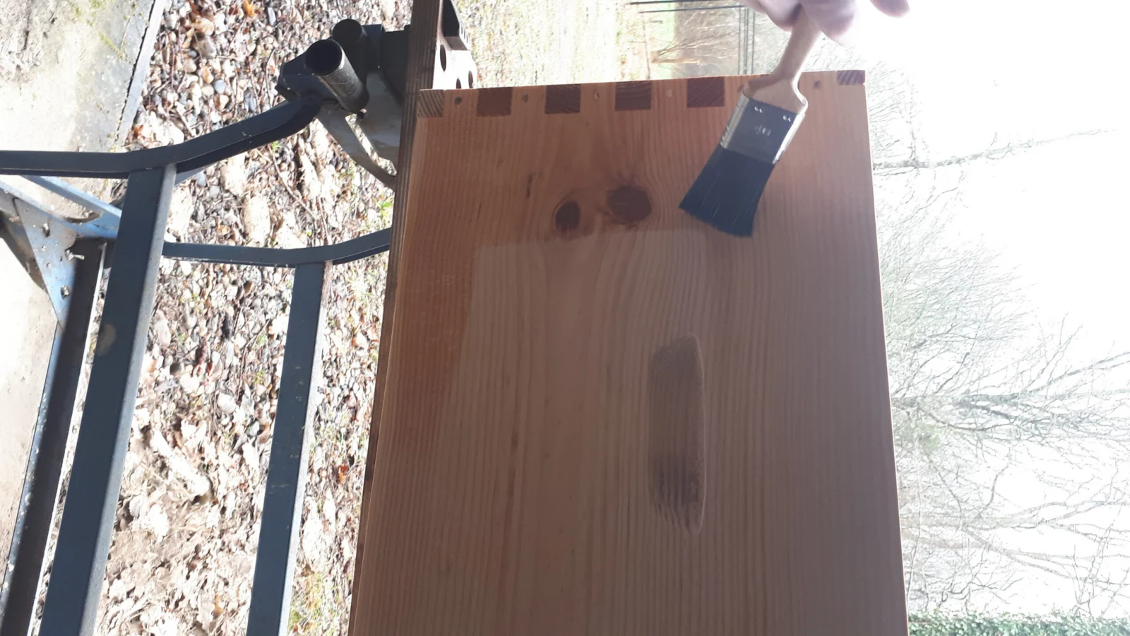 Corps de ruche Dadant en bois brut, angles assemblés en créneaux, un pinceau posé dessus.