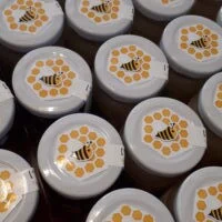 Couvercles de pots de miel ornés du logo de l'association : une abeille dans un cercle d'alvéoles.