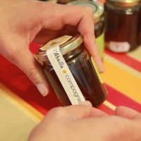 Mains posant une bande « L'Abeille de Compagnie » sur le couvercle d'un pot de miel.