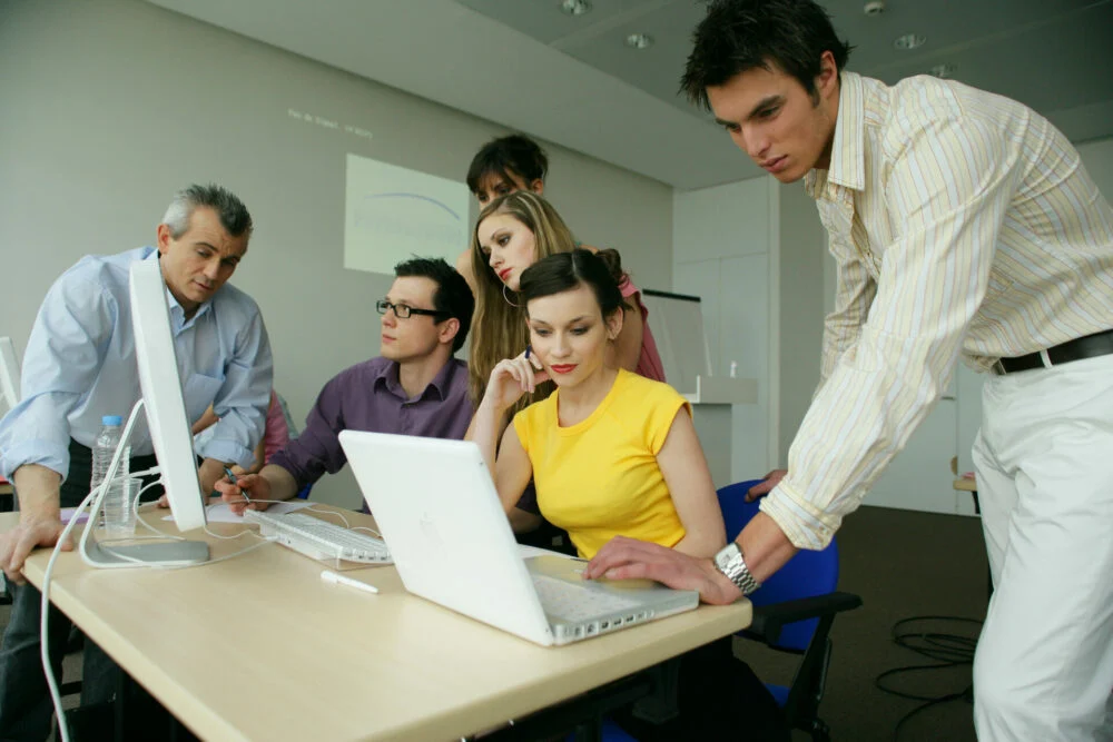 Cinq collègues réunis autour d'un ordinateur portable dans un bureau.