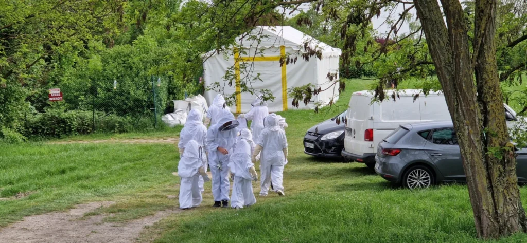 Groupe en combinaisons d'apiculteur dans une prairie, près d'une tente et de voitures.